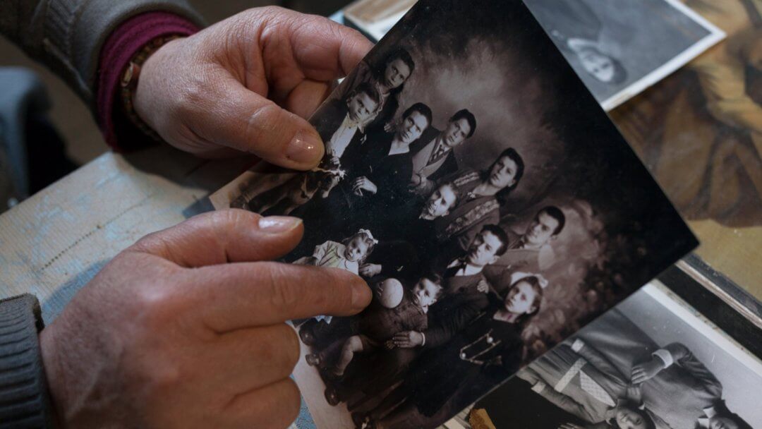 old hands of grandmother use an old photograph to point a child because she is discovering sicilian roots